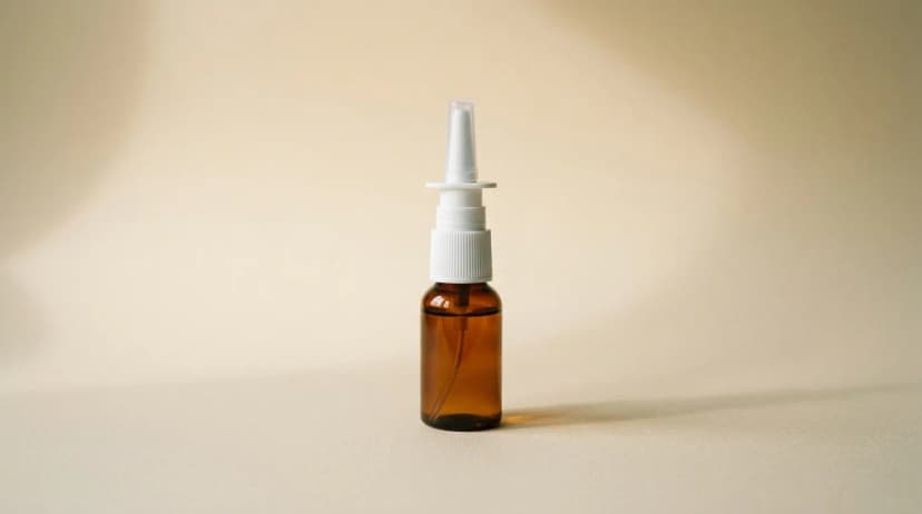 Amber-tinted nasal spray bottle with white pump cap on a warm cream surface.